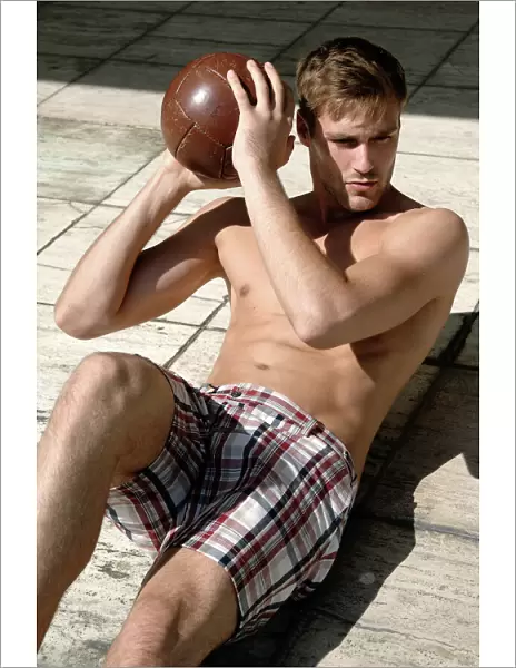 Athletic young man in shorts with ball lying on a stone floor