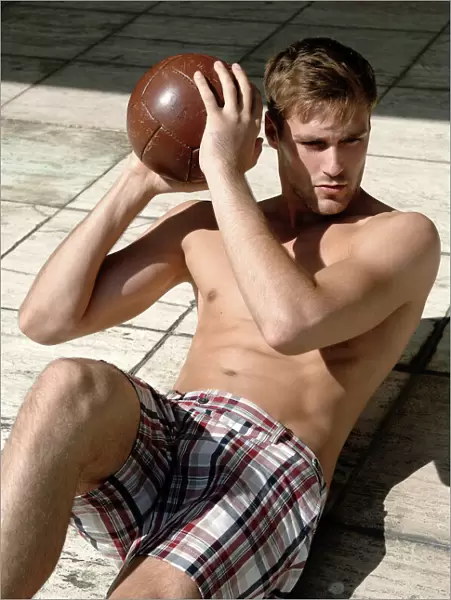 Athletic young man in shorts with ball lying on a stone floor