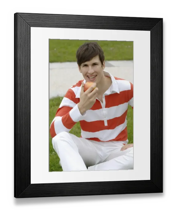 Framed Print : Young man sitting on a lawn eating an apple Framed Print : Young man sitting on a lawn eating an apple