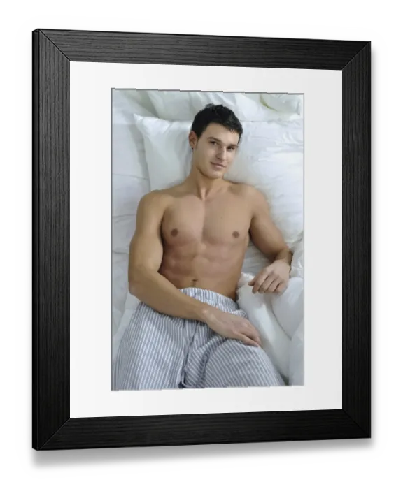 Framed Print : Bare-chested young man wearing pyjama bottoms lying in bed