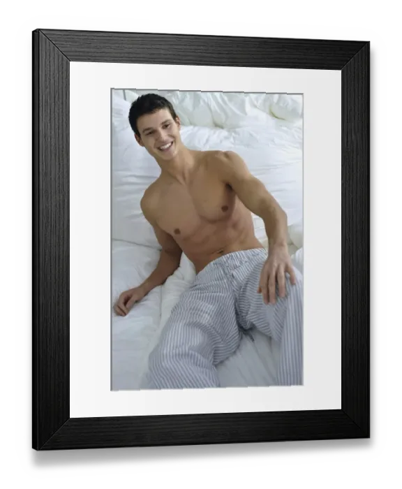 Framed Print : Bare-chested young man wearing pyjama bottoms lying in bed