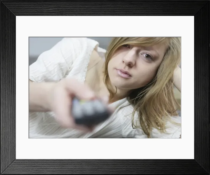 Framed Print : Young woman lying down with remote in her hand Framed Print : Young woman lying down with remote in her hand