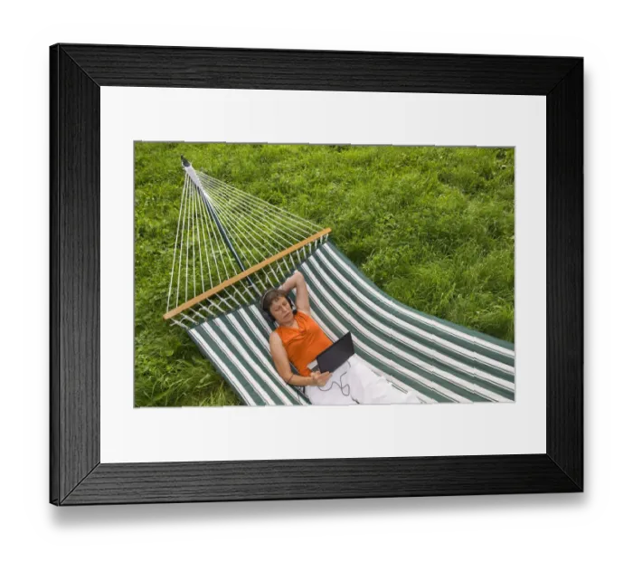 Framed Print : Senior woman with netbook and headset lying in a hammock Framed Print : Senior woman with netbook and headset lying in a hammock