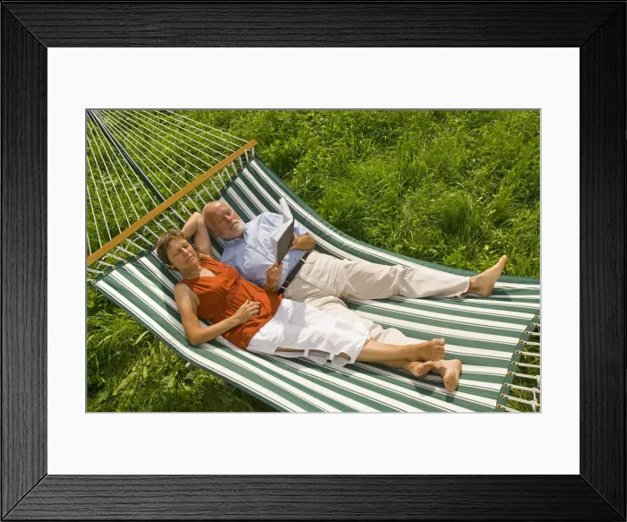Framed Print : Senior citizen couple lying in a hammock, woman listening to music, man reading a book Framed Print : Senior citizen couple lying in a hammock, woman listening to music, man reading a book