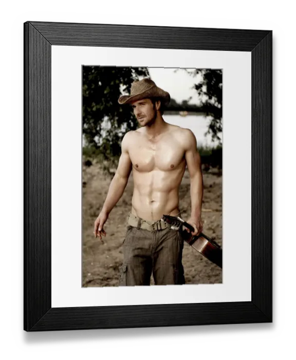 Framed Print : Masculine man without a shirt, wearing a cowboy hat and holding a guitar on a beach