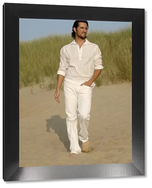 Man wearing white clothes walking in the dunes on the beach