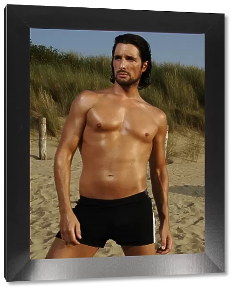 Muscular man wearing swimming trunks posing on beach