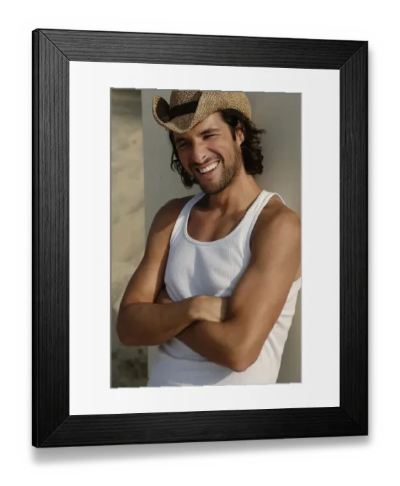 Framed Print : Man wearing a sun hat on a beach, leaning against a cottage, smiling