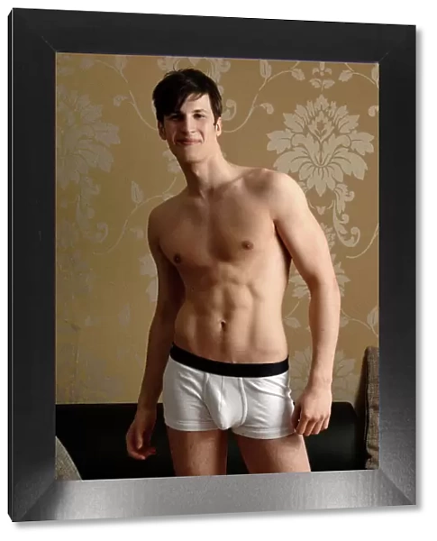 Young smiling man wearing underwear standing in front of nostalgic wallpaper