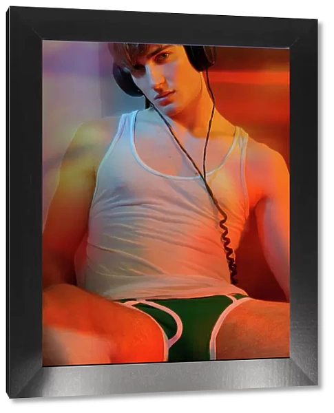 Young man in underwear with headphones in colorful light