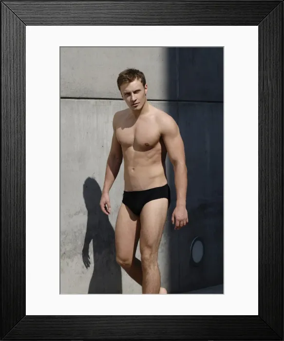 Framed Print : Young man wearing bathing trunks, walking in front of a concrete wall Framed Print : Young man wearing bathing trunks, walking in front of a concrete wall