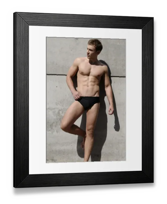 Framed Print : Young man wearing bathing trunks, leaning against a concrete wall Framed Print : Young man wearing bathing trunks, leaning against a concrete wall