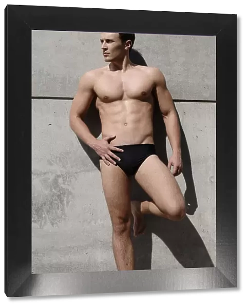 Young man wearing bathing trunks, leaning against a concrete wall