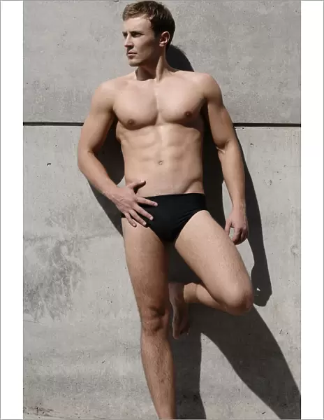 Young man wearing bathing trunks, leaning against a concrete wall