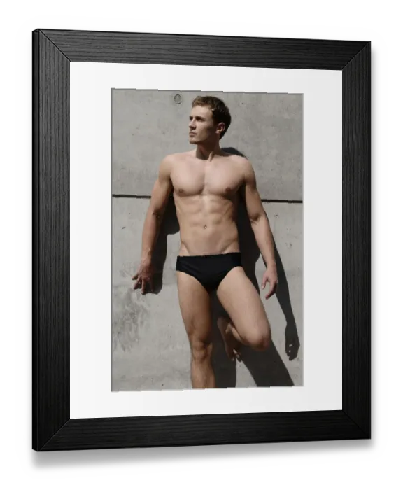 Framed Print : Young man wearing bathing trunks, leaning against a concrete wall