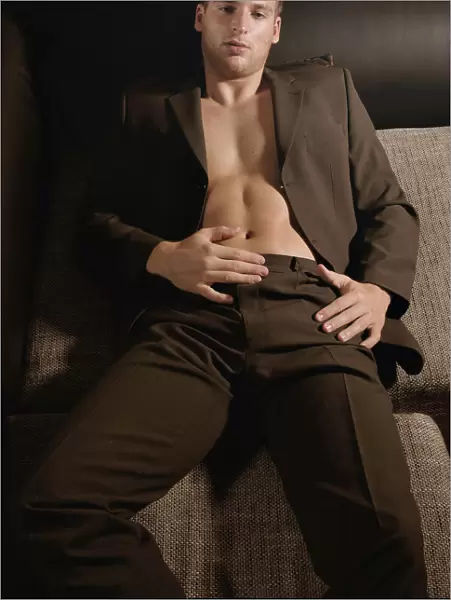 Young man in a suit and without shirt lying on a couch