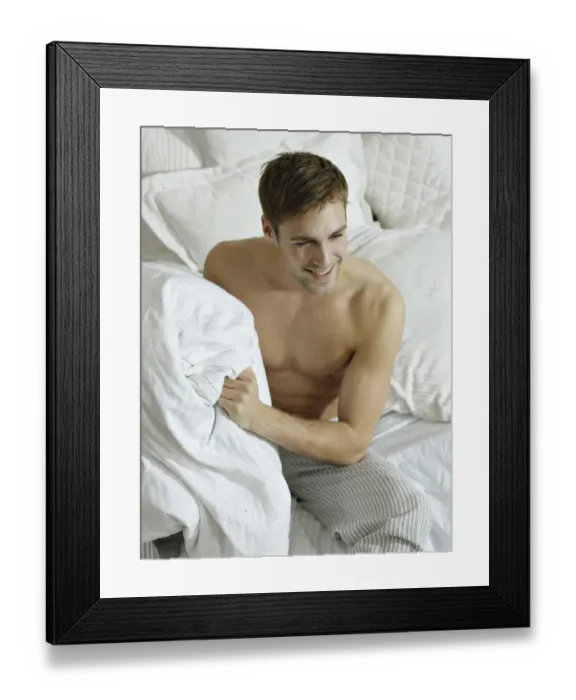 Framed Print : Charming bare chested man wearing pyjamas sitting on a bed, smiling Framed Print : Charming bare chested man wearing pyjamas sitting on a bed, smiling
