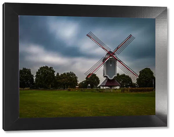 Traditional wind mill in Lomel, Belgium, with clouds and grass field, long exposure