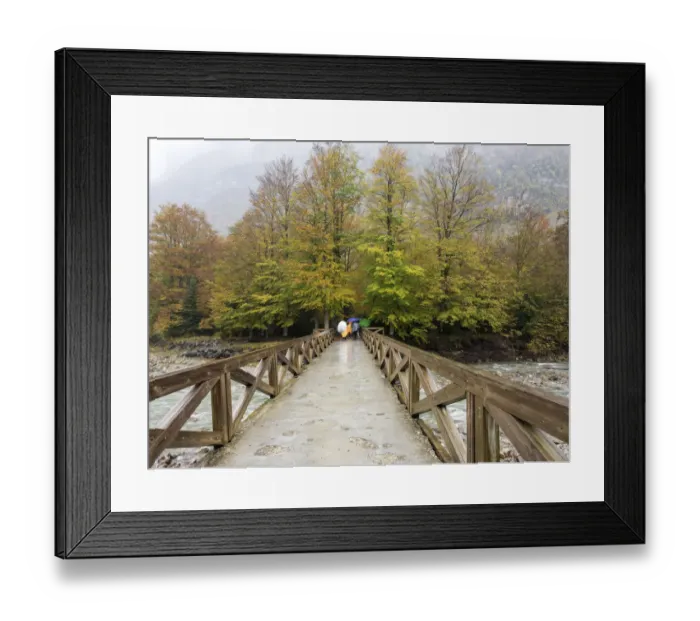 Framed Print : Persons with umbrellas that walk on a bridge of wood that crosses a river in a forest in autumn