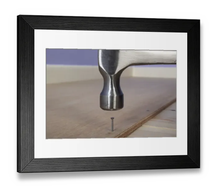 Framed Print : Hammering a ring-shank nail in to plywood on the floor