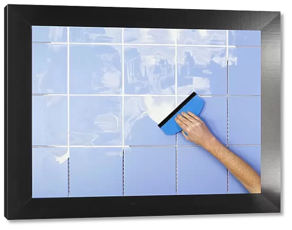 Hand spreading grout on tiles with grout spreader