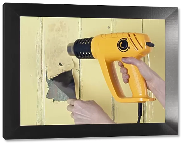 Using a heat gun and scraper to strip paint from a wooden surface