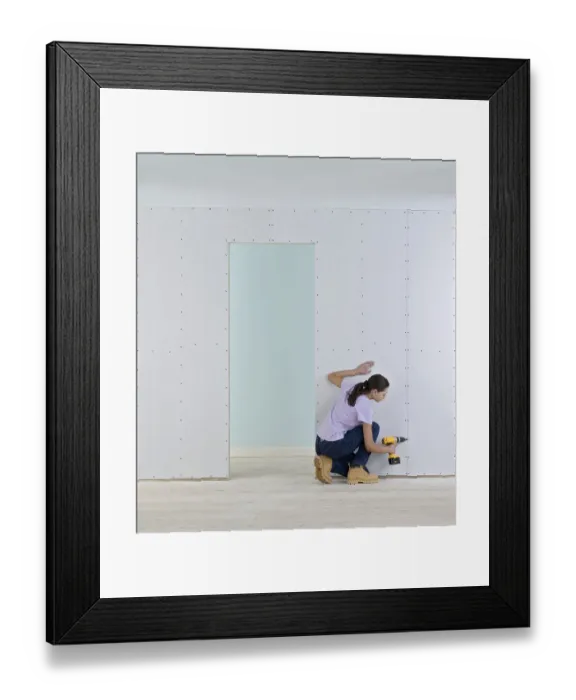 Framed Print : Woman holding screwdriver to wall of plasterboard Framed Print : Woman holding screwdriver to wall of plasterboard