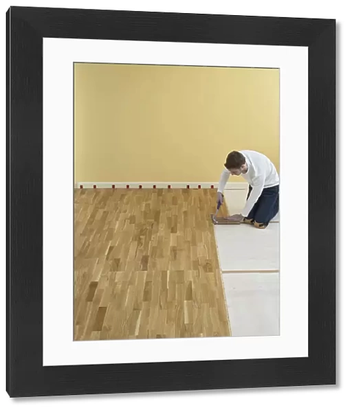 Man kneeling and holding hammer over floorboards