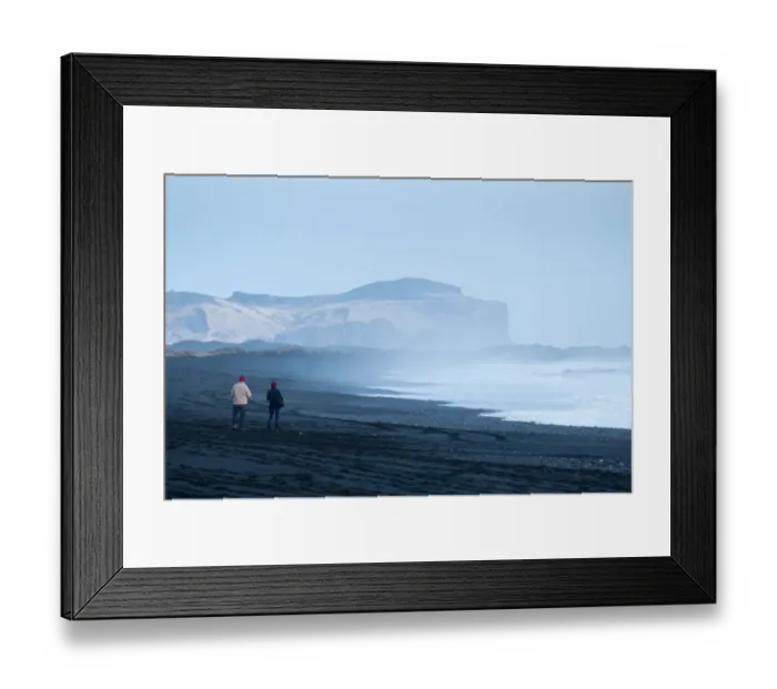 Framed Print : A couple are walking along the Viks black beach Framed Print : A couple are walking along the Viks black beach