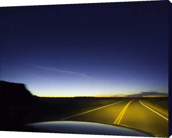 Road past sandstone buttes, lit by headlights, night (blurred motion)