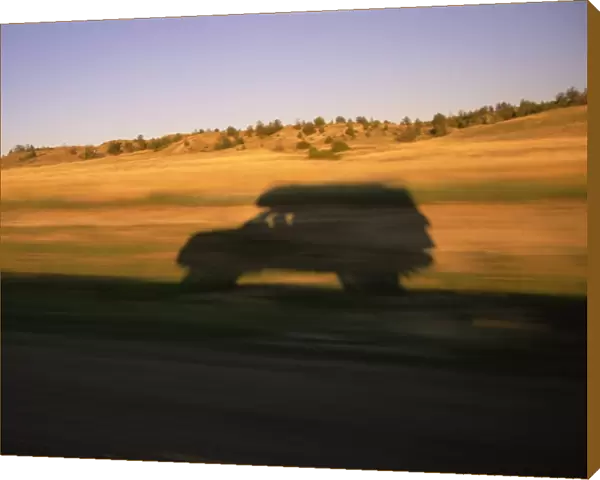 USA, Montana, SUV casting shadow on roadside, sunset (blurred motion)