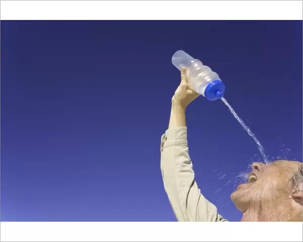 Mature man pouring water over face under clear sky, low angle view