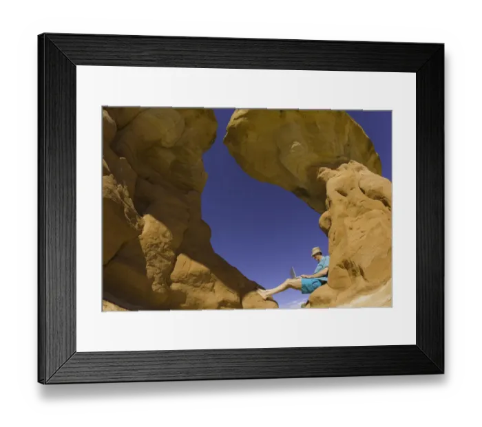 Framed Print : Mature man sitting on rock formation, working on laptop computer Framed Print : Mature man sitting on rock formation, working on laptop computer