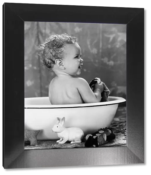 Baby with wet hair sitting in wash basin, smiling, taking a bath