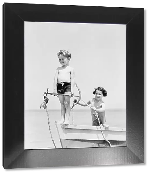 Boy standing on bow of row boat holding anchor, girl holding rope