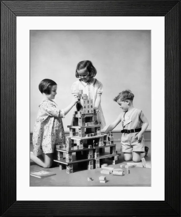 Framed Print : Two girls and one boy playing with alphabet building blocks constructing multi story structure Framed Print : Two girls and one boy playing with alphabet building blocks constructing multi story structure