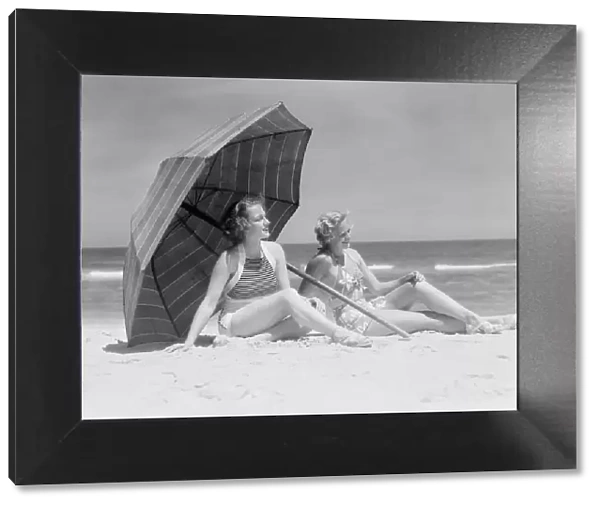 Two women sitting on beach under parasol
