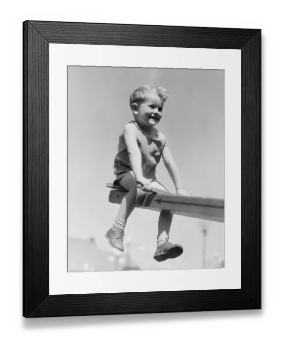 Framed Print : Boy sitting on see-saw in playground, legs dangling Framed Print : Boy sitting on see-saw in playground, legs dangling