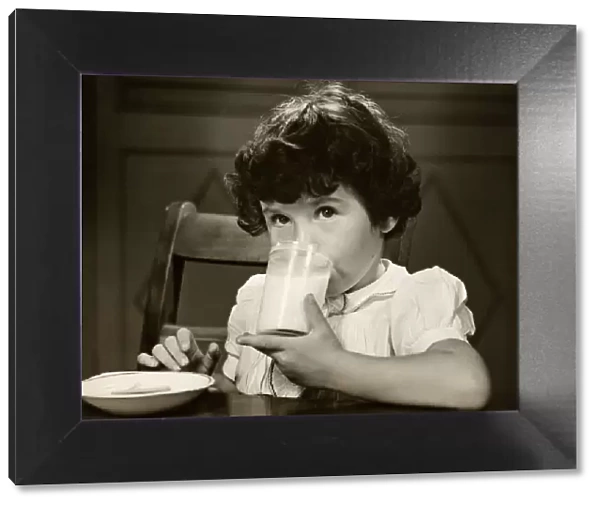 Little girl drinking a glass of milk at table