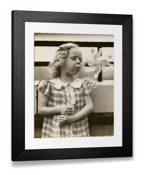 Framed Print : Little girl blowing on pin wheel toy Framed Print : Little girl blowing on pin wheel toy