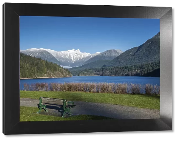 Snow-capped mountains above lake and meadow with bench, British Columbia, Canada