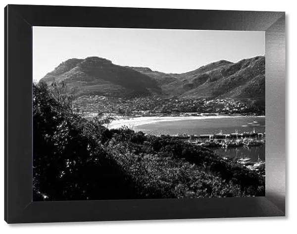 A black and white panoramic picture of Hout Bay with Hout Bay Beach on the left and the marina and fishing harbour in the foreground. Chapmans Peak is in the background. Western Cape Province, South Africa