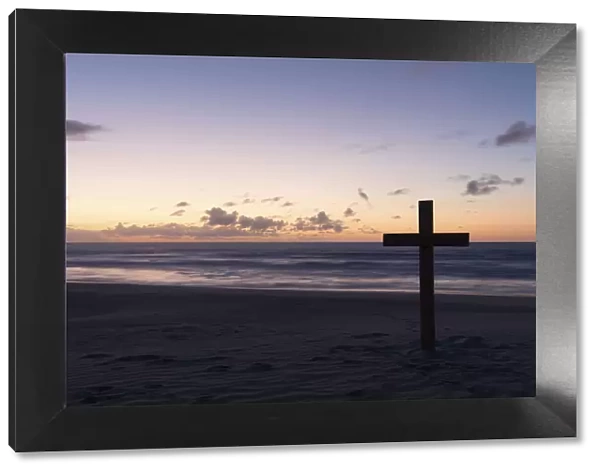 An old cross on sand dune next to the ocean with a calm sunrise - Arniston, South Africa