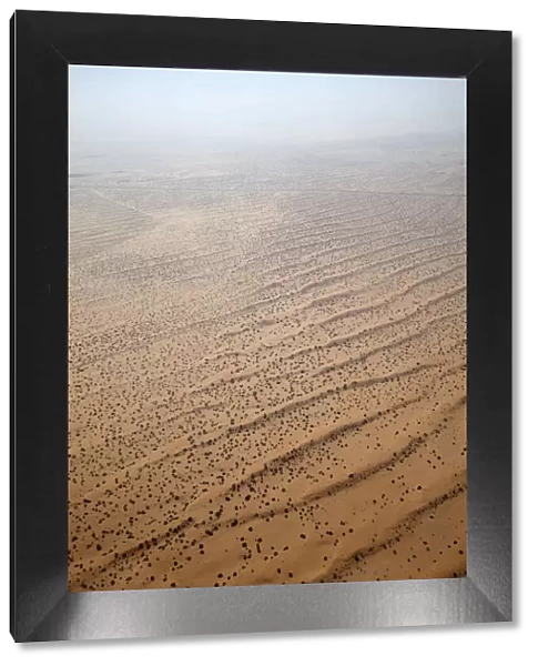 Flying over a settlement in the desert of the United Arab Emirates, with scattered habitation, a road and agriculture. The desert merges with the sky