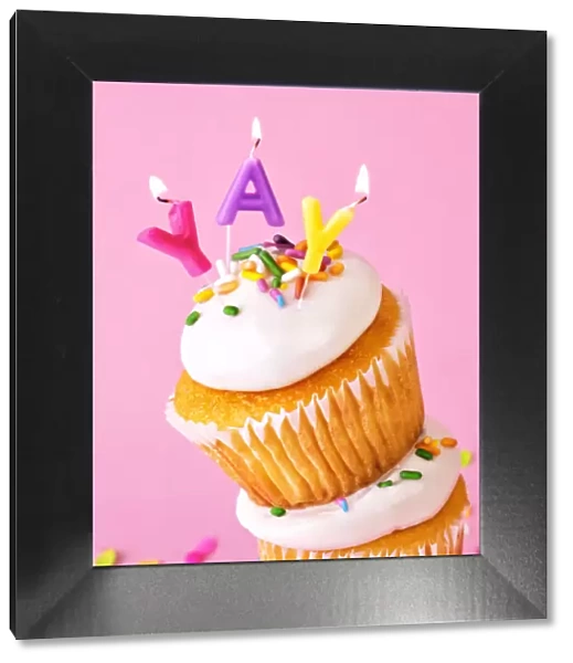 Frosted cupcakes with sprinkles and candles on pink background with confetti
