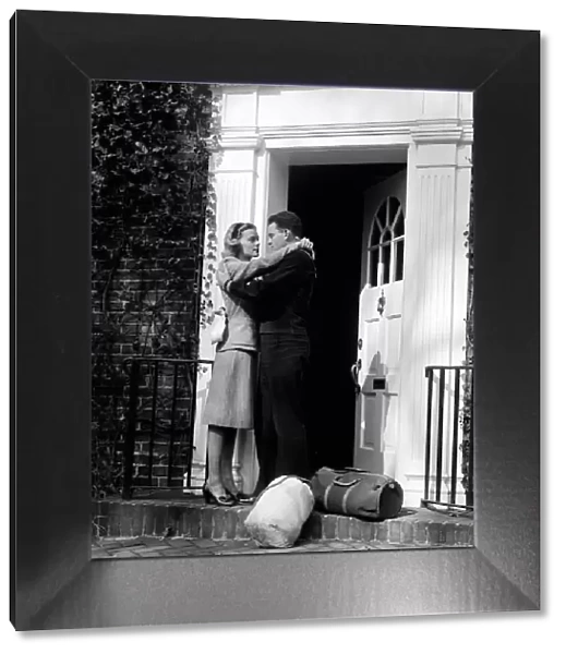 Sailor with duffel bags, hugging woman, about to kiss on front doorstep