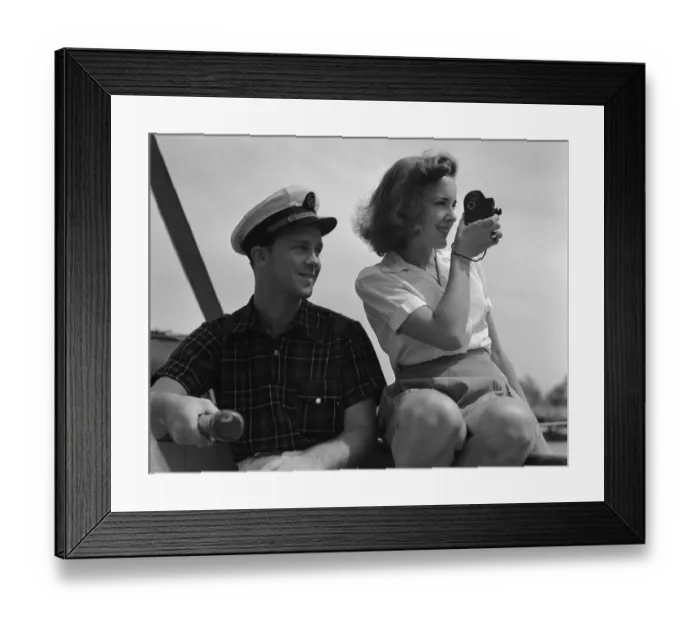Framed Print : Couple on sailing boat, man holding tiller, woman filming with movie camera. (Photo by H Framed Print : Couple on sailing boat, man holding tiller, woman filming with movie camera. (Photo by H