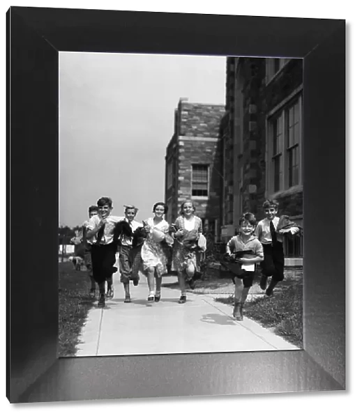 seven children running along pavement, outside schoolhouse