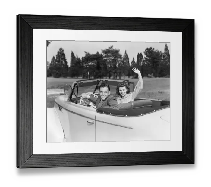 Framed Print : Teenage couple in convertible car smile and wave to viewer