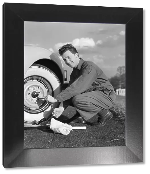 Smiling man in coveralls using tire iron to change tire on sedan
